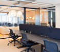 Office area, tables, chairs, sofa, glass walls, lamps, open floor plan.