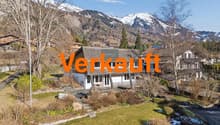 Detached house, white exterior, gray roof, surrounded by trees, mountains in the background, driveway