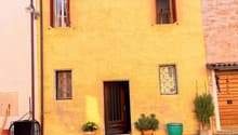 yellow brick building, wooden door, three windows, brick paved courtyard, plants