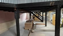 interior of a building, raised ground floor, corrugated metal roof, metal support beams, concrete floor, stack of wooden planks
