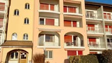 yellow apartment building with many balconies, red shutters, red roof, multiple floors, shrubs in front