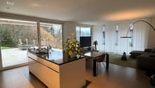 modern kitchen with central island, balcony with seating, large glass windows, dining table, green area with table, couch, television, large floor lamp