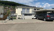 white house, concrete garage, cars parked, solar panels on the roof, fenced yard, mountains in the background