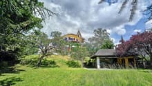 House on a hill, surrounded by trees, spacious lawn, small wooden house, steep stairs, white exterior, red trims