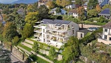 Modern white house with solar panels, multiple balconies, surrounded by trees and greenery, with a view of the mountains
