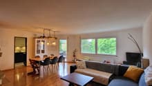 Living room with dining area, wooden floor, fireplace, sofa, coffee table, chandelier, dining table with chairs, window with view