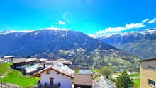Mountain village with several houses, snow-capped mountains, green fields, clear blue sky