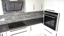Modern kitchen with white cabinets, black countertops, stone backsplash, built-in oven and dishwasher