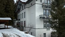 Two story building, snow covered ground, white building, wooden awning, balcony, attached garage
