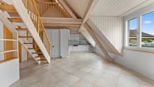A room with wooden beams, tiled floor, white cabinets, and a staircase.
