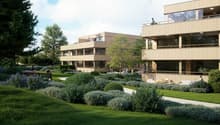 Two-story building with balconies, surrounded by a garden with various plants and trees.