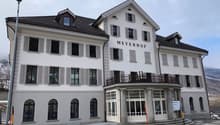 large white building, 'Meyerhof' text on front, large balcony with railing, many windows, white exterior, grey shutters, large arched windows on ground floor
