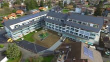 A multi-story school building with a large courtyard and parking area, surrounded by a residential neighborhood in a mountainous area.