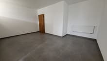 Empty room with white walls, a wooden door, and a radiator on the wall. The floor is covered with large gray tiles.