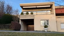 2 story building, raised ground floor, beige exterior, balcony, wooden door, large window, white planter