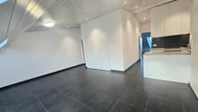Empty room with white walls, black tiled floor, white ceiling, two doors, kitchen area with countertop and cabinets