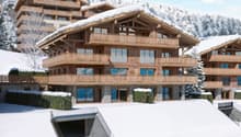 multi-level chalet with balconies, wooden exterior, set on a snowy hillside with a mountain backdrop