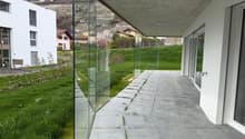 Modern building with glass walls, concrete ceiling, concrete pathway, green grass, mountain view