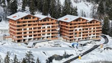 Two wooden apartment buildings, multiple floors, balconies, snow-covered surroundings, under construction