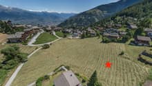 large open field for construction, surrounded by alpine houses and greenery, mountainous backdrop
