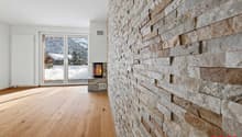 Spacious living room with a stone fireplace, large windows overlooking a snowy landscape, and hardwood flooring.