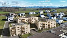 Aerial view of modern apartment buildings with green roofs and solar panels, located in a rural setting with surrounding green fields and mountain views.