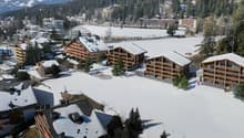 Building complex with multiple apartment buildings with snow on the ground and surrounding mountains.