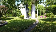 Contemporary house, white walls, glass windows, pathway, garden with green grass, trees, pink lounge chairs