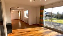 Large living room, hardwood floor, ceiling lights, large windows with curtains, sliding doors to balcony