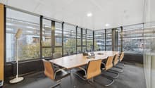 modern office with carpet, large windows, a long desk, modern chairs, a laptop, and a white lamp