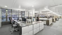 modern office layout with desks, black office chairs, monitors, keyboards, large windows