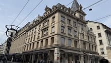 The image shows a large, ornate multi-story building with a prominent tower and decorative architectural features. The building has a Longchamp store on the ground floor and appears to be located on a busy city street with tram lines and pedestrians visib
