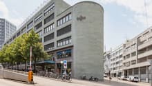 Regus building, multiple floors, glass windows, bicycles parked outside, trees, cars parked on the street