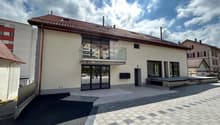 2-story building with a red tiled roof, large windows, and a balcony on the upper floor. The building has a modern, minimalist design with a paved outdoor area in front.