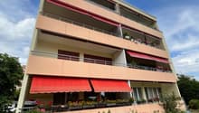4 story apartment building, beige walls, red awnings, balconies with plants