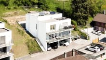 3-story modern white house with balconies, garage, and parking spaces, surrounded by trees and greenery