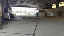 empty warehouse with concrete floor, metal roofing, large open space, some equipment, brick walls, windows, door on the right side
