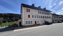 3 story building, beige and brown exterior, multiple windows, 2 garages, 2 cars parked in front