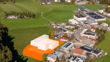 Proposed building outlined on a green field, with many houses and buildings in the background, a few solar panels installed.