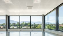 Large open office space with floor-to-ceiling windows offering a panoramic view of the surrounding mountains and greenery. The space features a clean, modern design with a tiled floor, recessed lighting, and a minimalist aesthetic.