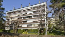 large building with many apartments, multiple floors, white exterior, brown accents, multiple windows, surrounded by greenery
