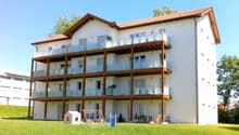 White apartment building with multiple balconies, red roof, large grassy area in front