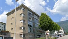 4 story building, glass windows, beige exterior, street light, trees, cars parked