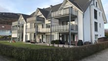 3 story apartment building, white exterior, gray roof, multiple balconies, garden, paved walkway