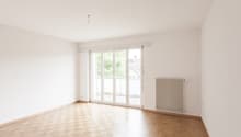 large room with white walls, wooden floor, sliding glass doors leading to a balcony, white radiator