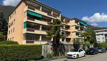 multi-story building, beige exterior, green awnings, balconies, hedges, palm tree, cars parked