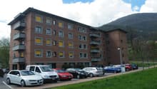 4-story building, red brick, many windows, several cars parked, grassy area, street light