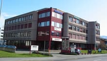 Office building, red facade, multiple windows, multiple floors, signboard, cars parked in front