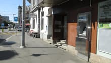 Building exterior with ATM, steps leading to entrance, sign for Zurich Kantonalbank, benches, and a streetlight.