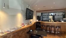 A room with a wooden floor, a counter, a table, chairs, a television, and a refrigerator.